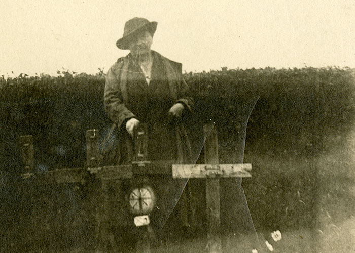 Sepia-coloured photograph of a woman standing outdoors next to several wooden grave markers.