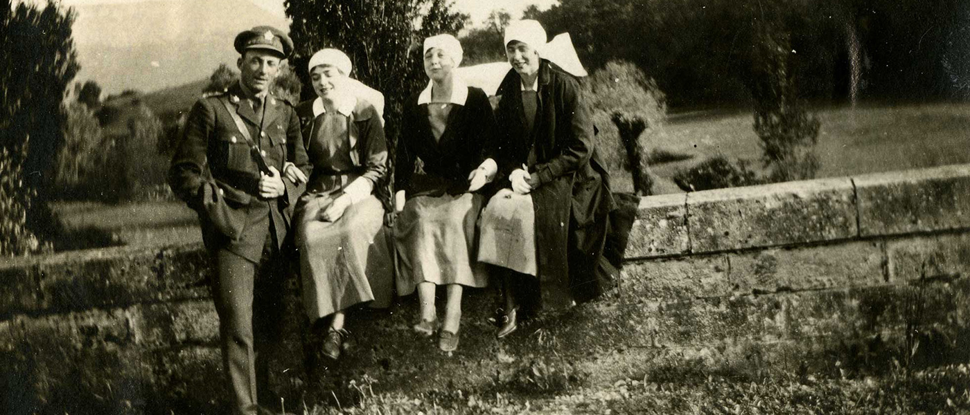 Black and white photograph of a soldier and three nursing sisters in uniform, sitting outdoors on a stone wall in France.