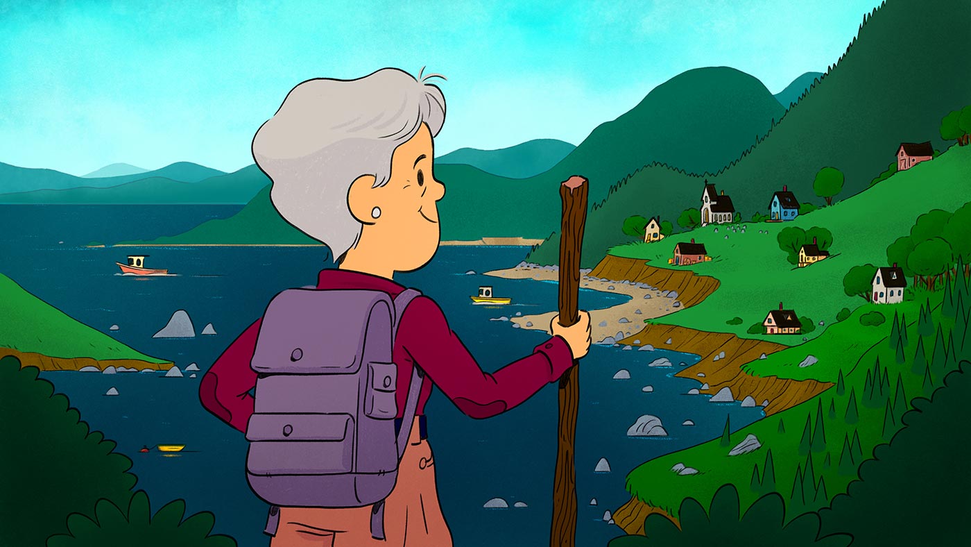 An older Helen Kendall is at the forefront wears bright hiking clothing, a backpack and holding a hiking stick. She is standing on a hillside overlooking a mountainous coastal view dotted with homes, and with three boats in the water. 