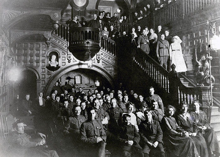 Black and white photograph of women and men in a foyer of a large estate house. Some men and women are in military uniforms.
