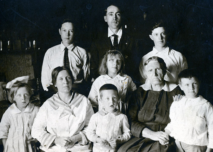 Photographie en noir et blanc de deux femmes et sept enfants qui posent pour la photo. Les garçons les plus âgés sont debout derrière les femmes de la photographie. Il y a quatre enfants dans la rangée avant, et leur mère et grand-mère sont assises.