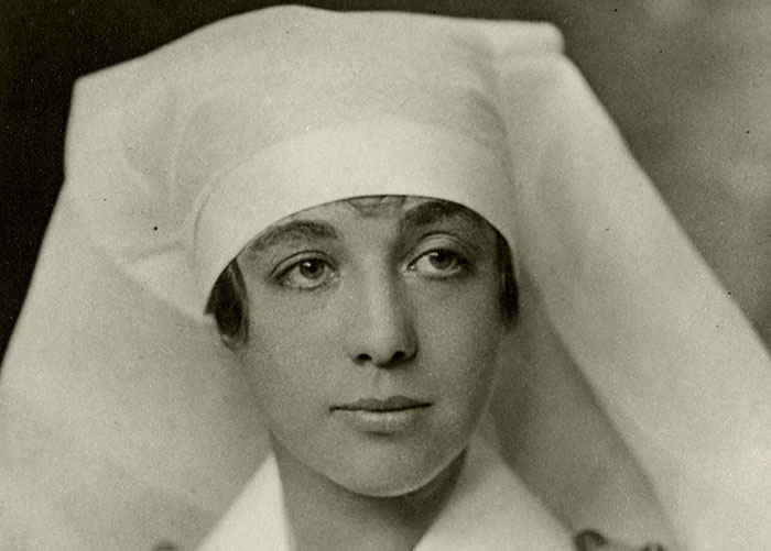 Photographie en noir et blanc de Helen Mary Kendall dans un uniforme d’infirmière. Elle a environ 27 ans et porte une coiffe d’infirmière blanche et une robe de coton avec des boutons en laiton, un tablier blanc et un grand collet blanc.